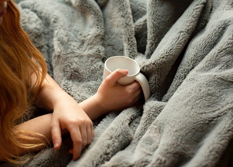 person covered in blanket and holding mug